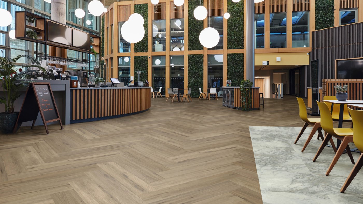Herringbone Leyster Oak lvp floors zone the walkway and cafe area in a university lounge while Sillano Marble lvt floors separate out the cafe seating and study area
