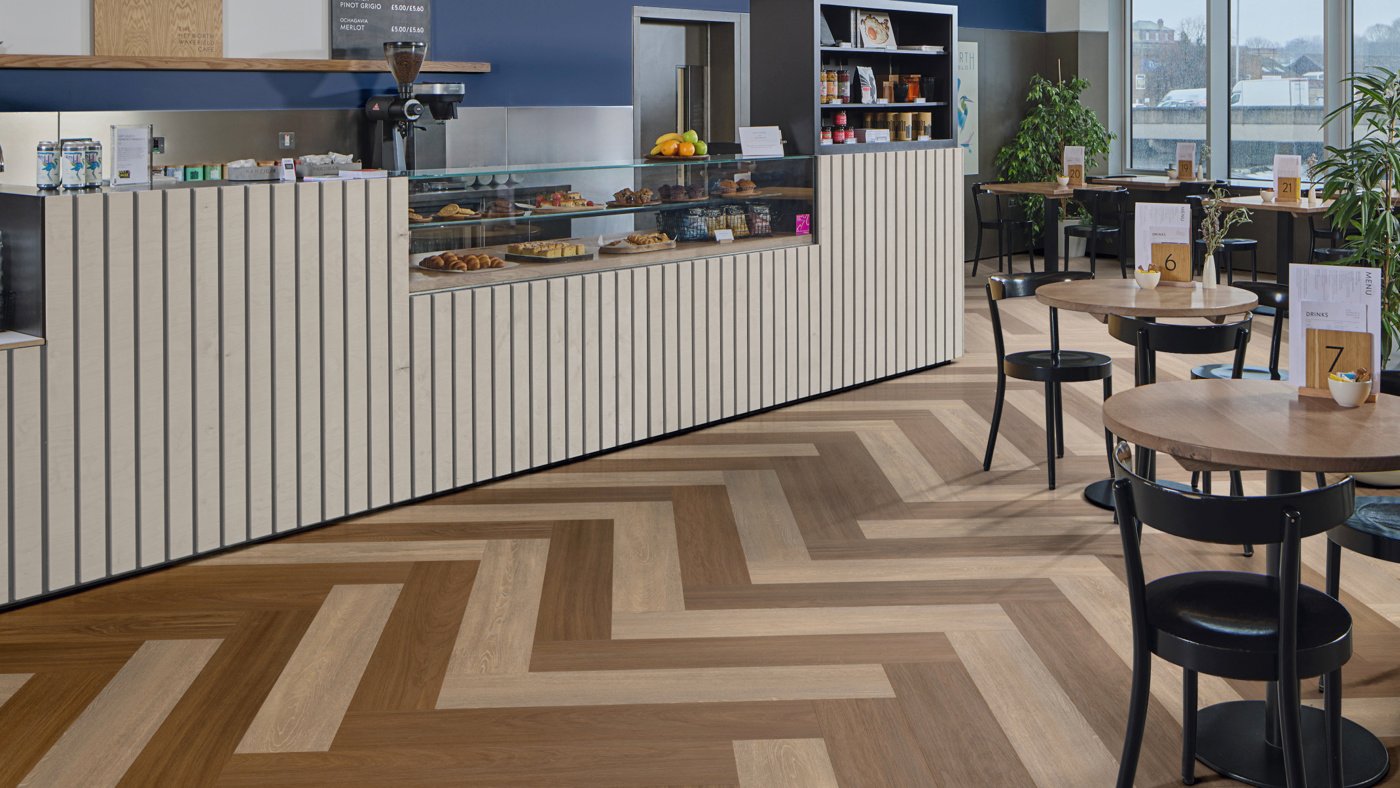 Barolo Oak and Niveus gluedown wood luxury vinyl plank flooring in a herringbone pattern adds cosiness and fun to a cafe and coffee shop